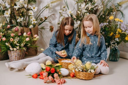 Two girls in a beautiful Easter photo zone with flowers, eggs, chickens and Easter bunnies. Happy Easter holiday.
