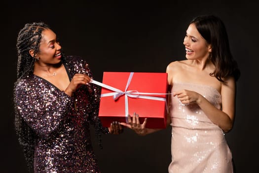 Joyful excited diverse ladies in nice outfits opening Christmas present