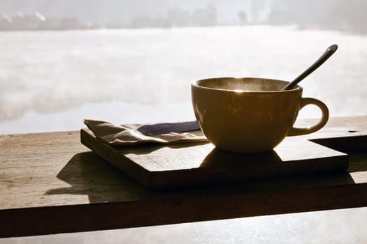 Coffee cup and napkin on wooden table in morning light