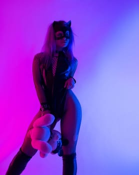 Sexy girl in a latex BDSM mistress dress and a cat mask in neon light on a dark background for a sex game