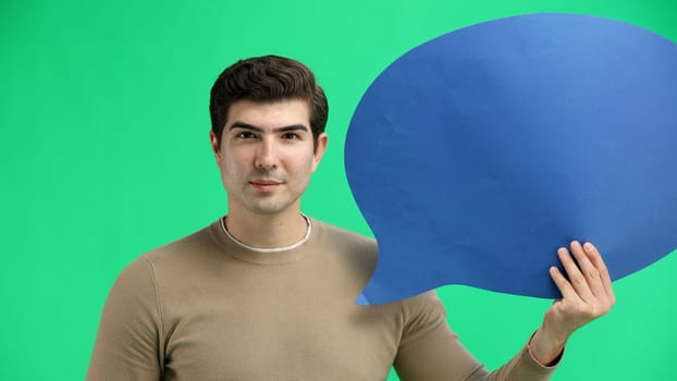 A man, close-up, on a green background, shows a blue comment sign