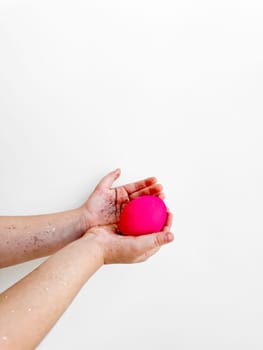 Hands holding a pink egg with glitter, Easter preparation and festive activity concept on a white background with copy space. For Easter themed creative content, and family activity ideas.