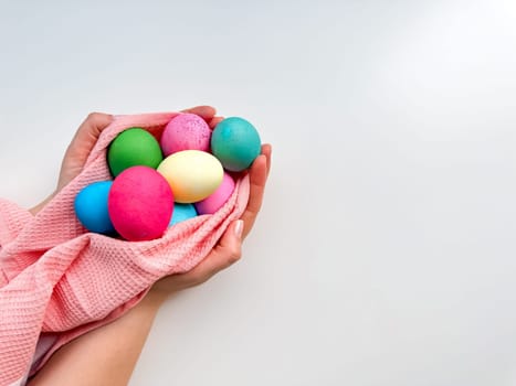 Hands tenderly hold variety of colorful Easter eggs wrapped in soft pink fabric on white background with empty space for text. Suitable for seasonal celebrations and festive spring looks.