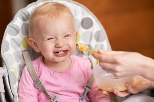 Happy, baby and laughing from feeding in high chair at home in the morning ready for eating food. Youth, funny and smile of a infant with development and laughter in house with fun and joy of a child