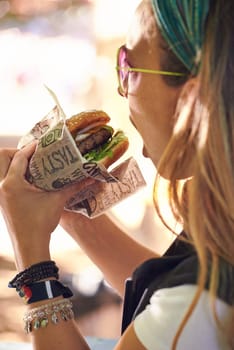 Face, fast food and woman eating burger closeup outdoor for hunger, takeaway or craving in summer. Hamburger, lunch or snack with head of hungry young person biting a beef bun for cuisine or meal.