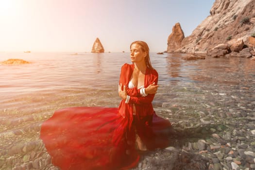 woman sea red dress. Beautiful sensual woman in a flying red dress and long hair, standing in sea in a large bay.