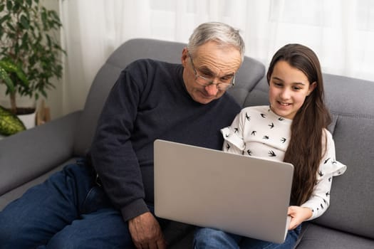 Happy retirement grandfather and pretty granddaughter laughing while watching e-book for learning to education together by laptop. Family educational at home concept. Technology and education.