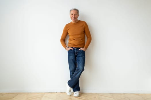 Positive grey-haired senior man posing on white wall background