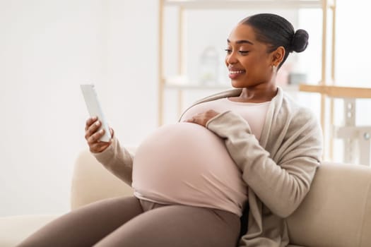 Smiling pregnant african american woman websurfing on smartphone