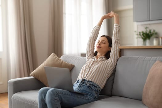 Relaxed young woman stretching on sofa with laptop