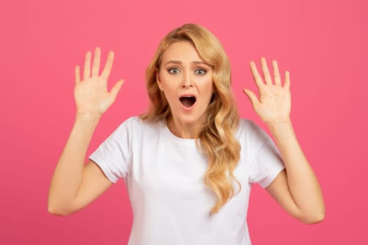 Shocked emotional blonde woman got caught with raised arms, studio