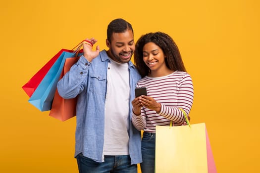 Shopping App. African American Couple Holding Shopper Bags And Using Smartphone