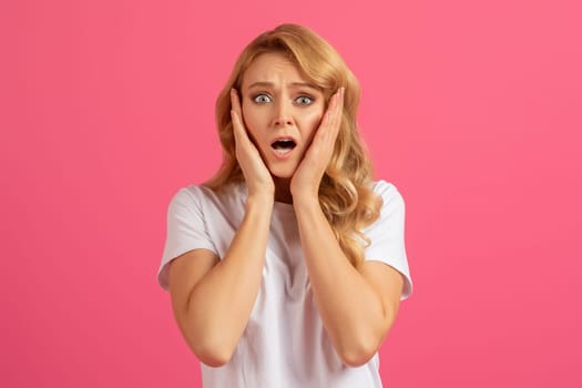 Young emotional blonde woman holding her face in shock, studio