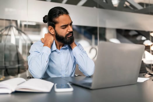 Exhausted young indian man employee suffering from office syndrome