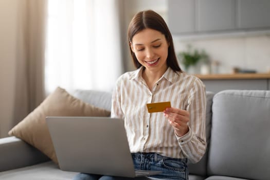 Happy young woman with credit card and laptop on sofa