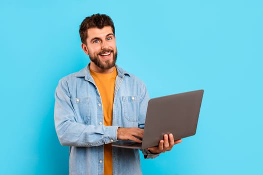 Cheerful millennial man casually dressed browsing internet on laptop, studio