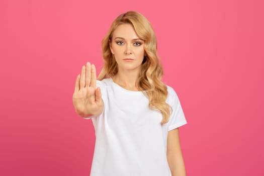 Determined young blonde lady gesturing stop with hand, portrait shot