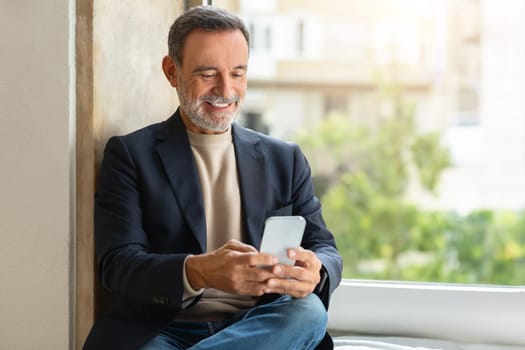 Smiling older man using a smartphone by the window