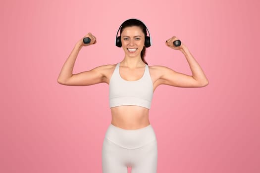 Joyful woman with a beaming smile flexing her muscles wearing headphones
