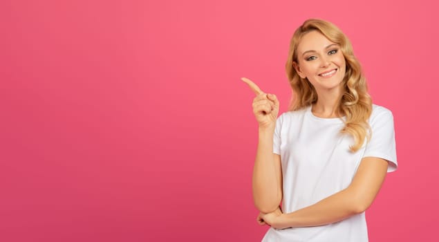 Positive Blonde Young Lady Pointing Finger Aside Over Pink Backdrop