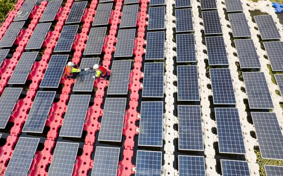 Wide shot and top view of two technician workers check and maintenance solar cell panel over the water reservoir as solar farm factory.