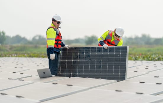 Two professional technician workers stand and hold solar cell panel in area of network of base over area of water reservoir.
