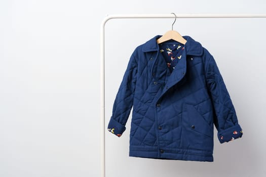 Blue quilted kids coat on hanger against white wall