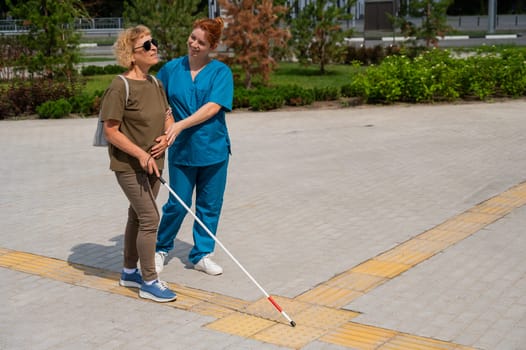 A nurse accompanies an elderly blind woman on a walk.