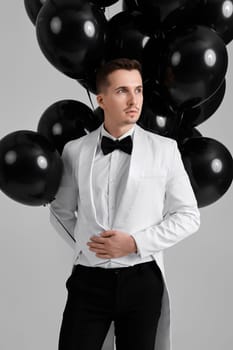 elegant businessman in suit tuxedo holding bunch of helium ballons on white background. Celebration