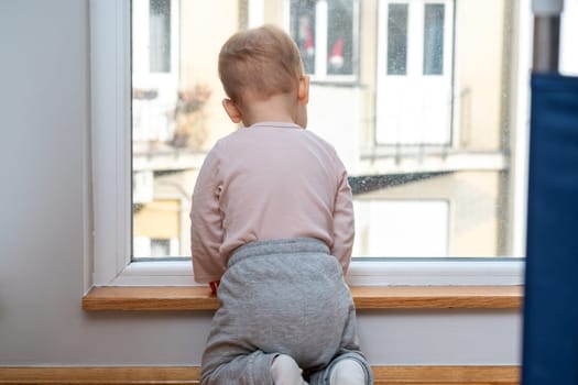 Adorable baby girl looking through the window. Stay home concept