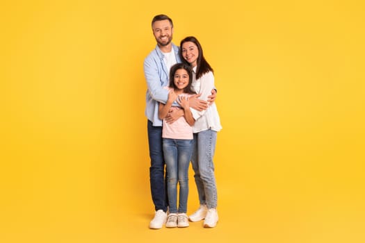 Joyful European family in casual hugging on yellow studio backdrop