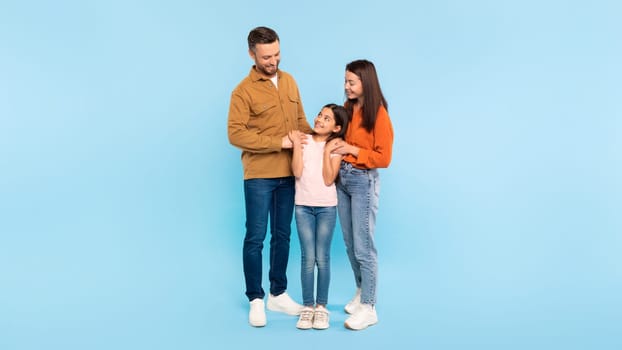 Cheerful parents with their kid daughter pose on blue backdrop