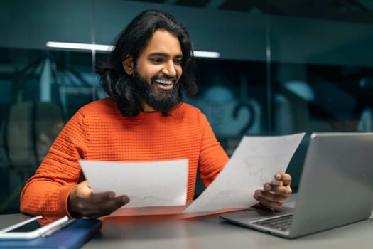 Happy millennial indian manager checking report at office