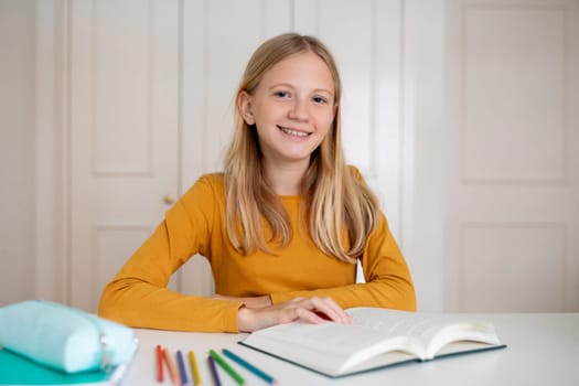 Smiling teenage girl sitting at desk with an open book at home