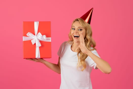 blonde woman in festive hat holding present box shouting, studio