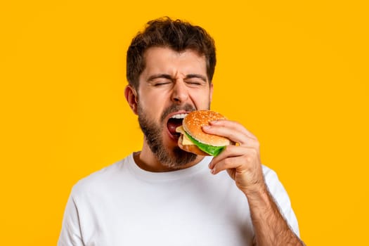 Funny man takes bite of tempting burger on yellow backdrop