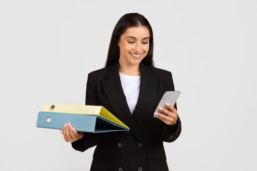 Smiling businesswoman multitasking with folders and smartphone