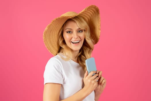 Happy tourist lady in summer straw hat using smartphone, studio