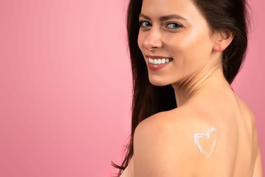 Radiant young woman with a heart-shaped lotion application on her shoulder