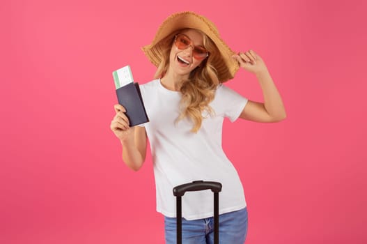 blonde woman posing with passport and boarding pass, pink backdrop