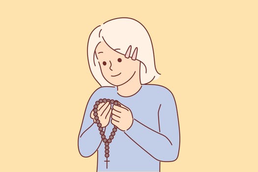 Little christian girl holding rosary with cross and praying, concept receiving religious education