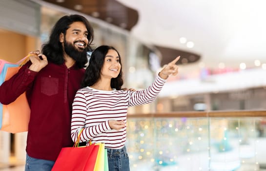 Affectionate young eastern couple standing in shopping mall with purchases