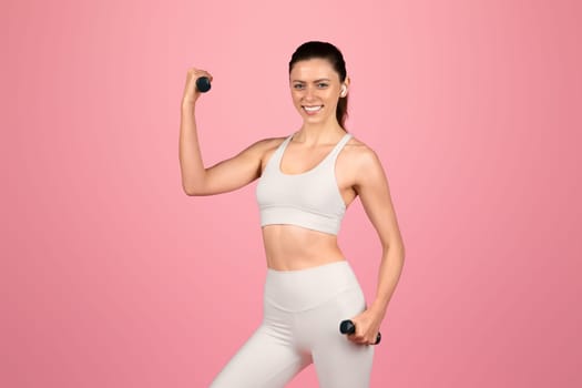 Enthusiastic fit woman in white workout gear happily exercising with dumbbells