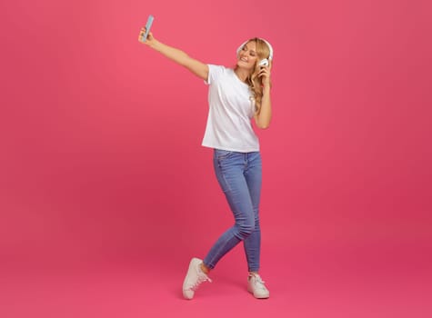 blonde woman wearing earphones making selfie on mobile phone, studio