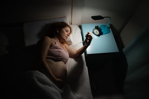 A pregnant woman lies in bed and uses a smartphone. Insomnia.