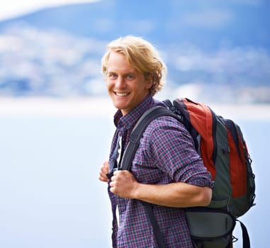 Man, trekking and portrait on mountains for travel, adventure and wellness by ocean, sea and vacation in Europe. Face of an excited, young person with backpack for hiking, explore and outdoor journey