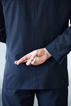 Businessman, back and fingers crossed with luck for hope, confidential or secret on a studio background. Closeup or rear view of man or business employee hiding hand in conspiracy, lie or corruption