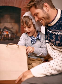 Father, son and opening gift on Christmas, curiosity and happy for celebrating a festive holiday. Daddy, child and bonding on religious vacation in living room, childhood and tradition of present