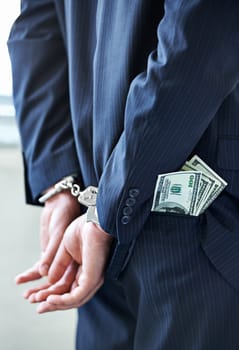 Business person, hands and cash with handcuffs for bribe, secret or corruption in financial crime. Closeup or rear view of employee with pocket money, paper or laundering finance in bribery or fraud