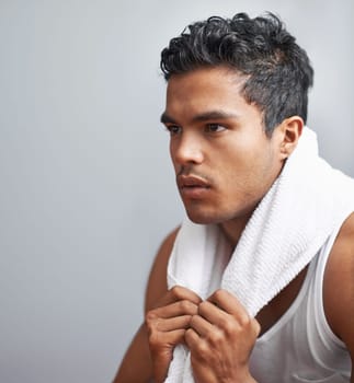 Face, fitness and towel with man breathing in studio isolated on gray background for workout. Exercise, sweating and intensity with confident young athlete on break from training for performance